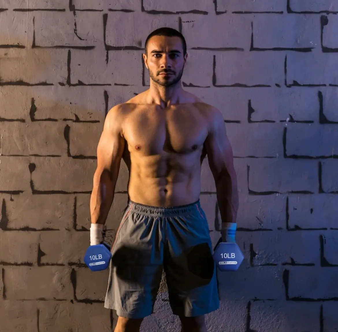Man with dumbbells in front of brick wall.